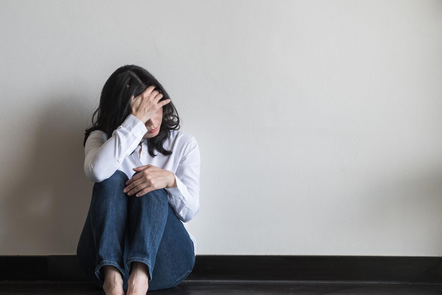 Anxiety disorder menopause woman, stressful depressed, panic attack person with mental health illness, headache and migraine sitting with back against wall on the floor in domestic home