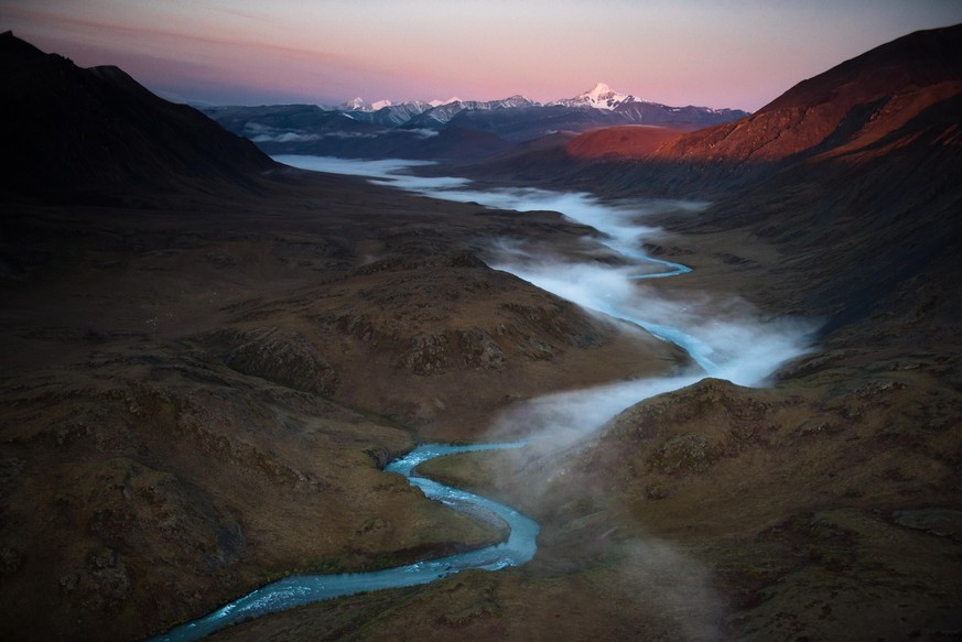 Fog is rising from the Hula Hula river in the early morning hours. In the background rises Mount Chamberlin, the third highest peak in the Brooks Range.