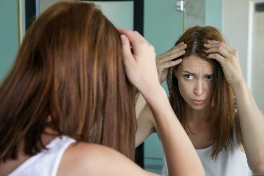 Macht vielen Menschen Sorgen: Eine Frau überprüft vor dem Spiegel, ob sie schon graue Haare bekommt. 
