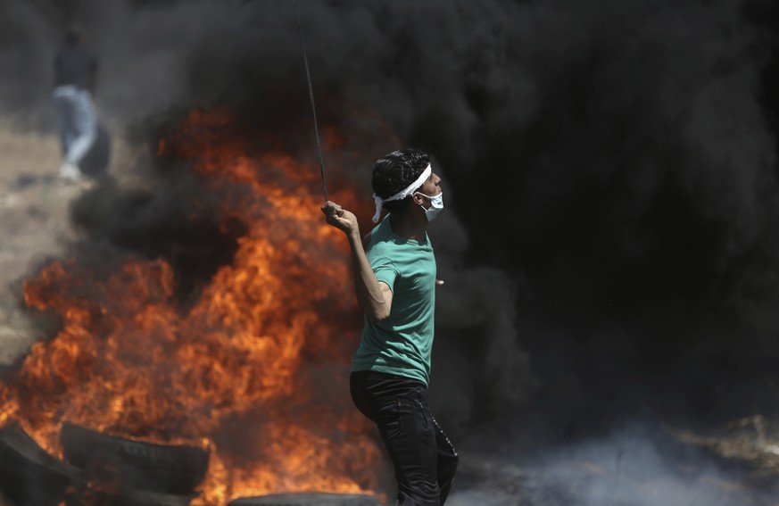 A Palestinian protester hurls stones at Israeli troops during a protest at the Gaza Strip&#039;s border with Israel, Monday, May 14, 2018. Thousands of Palestinians are protesting near Gaza&#039;s bor ...