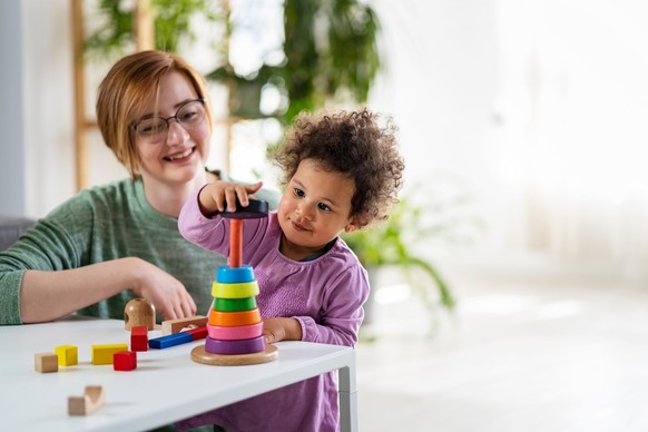 Mother looking at a child playing with an educational didactic toy. Preschool teacher with a child playing with didactic toys. Mixed race family