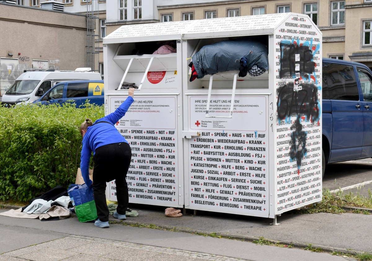 Eine Frau befuellt in Berlin einen Altkleider -Container des DRK mit Kleidungsstuecken *** A woman fills a DRK container with old clothes in Berlin