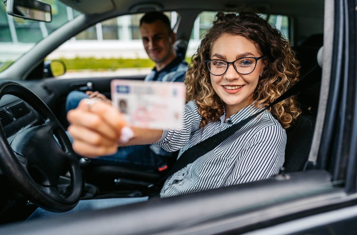 Portrait of a female student passing her driving test after a young driving instructor graded her. Holding her new driver&#039;s licence.
