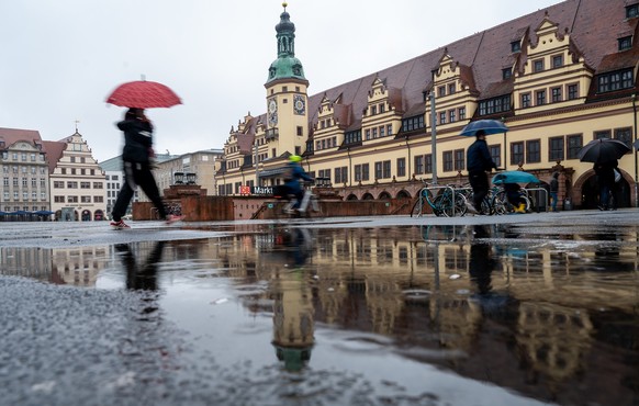 16.04.2023, Sachsen, Leipzig: Das Alte Rathaus in Leipzig spiegelt sich in einer gro�en Pf�tze auf dem Markt. Tr�bes Wetter mit viel Regen bestimmte dieses Aprilwochenende. Foto: Hendrik Schmidt/dpa + ...