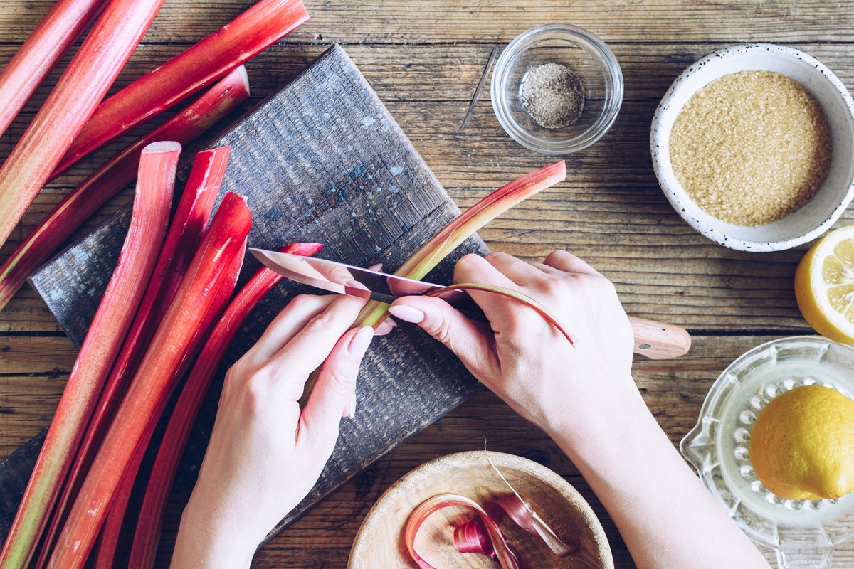 Woman preparing fresh picked stalks of organic rhubarb for cooking on a wooden background. Step by step recipe of poached rhubarb. Series. Top view.