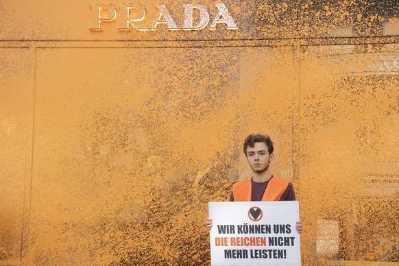 22.04.2023, Berlin: Ein Aktivist der Umweltschutzgruppe Letzte Generation hält vor einem Luxusgeschäft ein Plakat. Zuvor hatte er die Fassade mit Farbe besprüht. «Die reichsten Deutschen emittieren ta ...