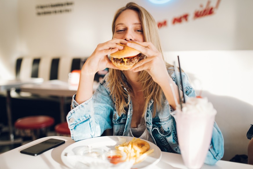 Young woman eating burger in restaurant