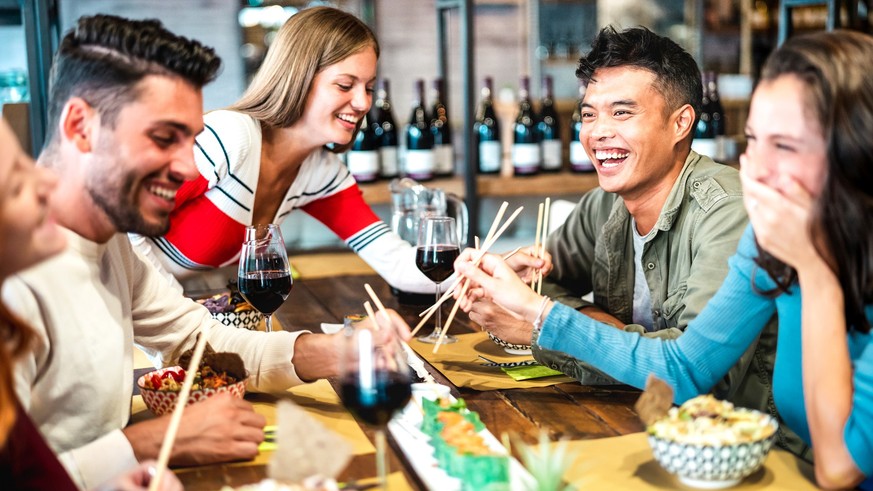 Multicultural trendy friends eating sushi with chopsticks at fusion restaurant bar - Food and beverage life style concept with happy young people having fun together at cool eatery - Vivid filter