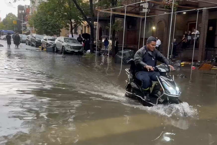 In this photo taken from video, a man drives a scooter through flood waters, Friday, Sept. 29, 2023, in the Brooklyn borough of New York. A potent rush-hour rainstorm has swamped the New York metropol ...