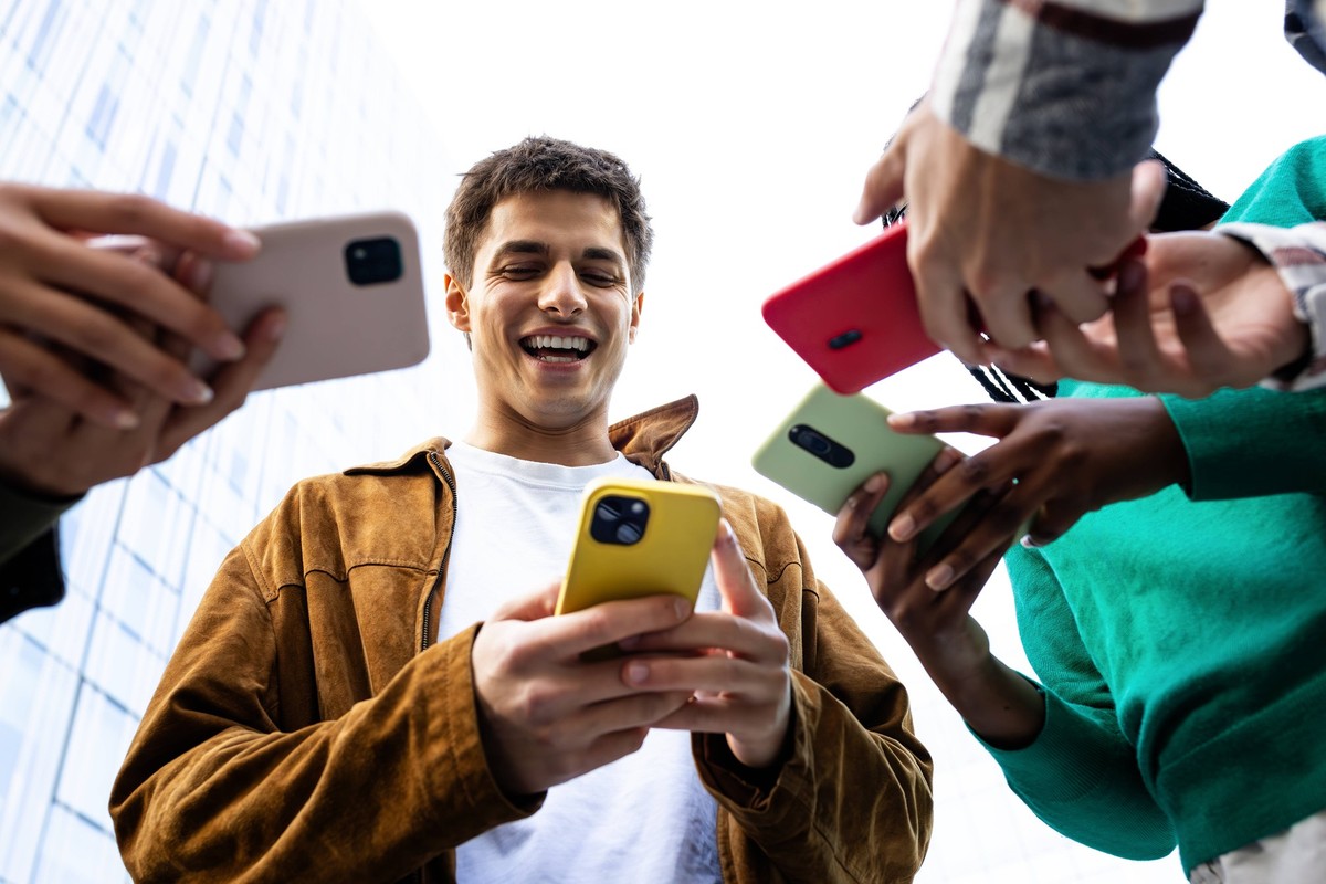 Young man showing smartphone content to his friends outdoors Group of friends using smartphones, sharing content and having fun together outdoors, model released, , 98203740.jpg RECORD DATE NOT STATED