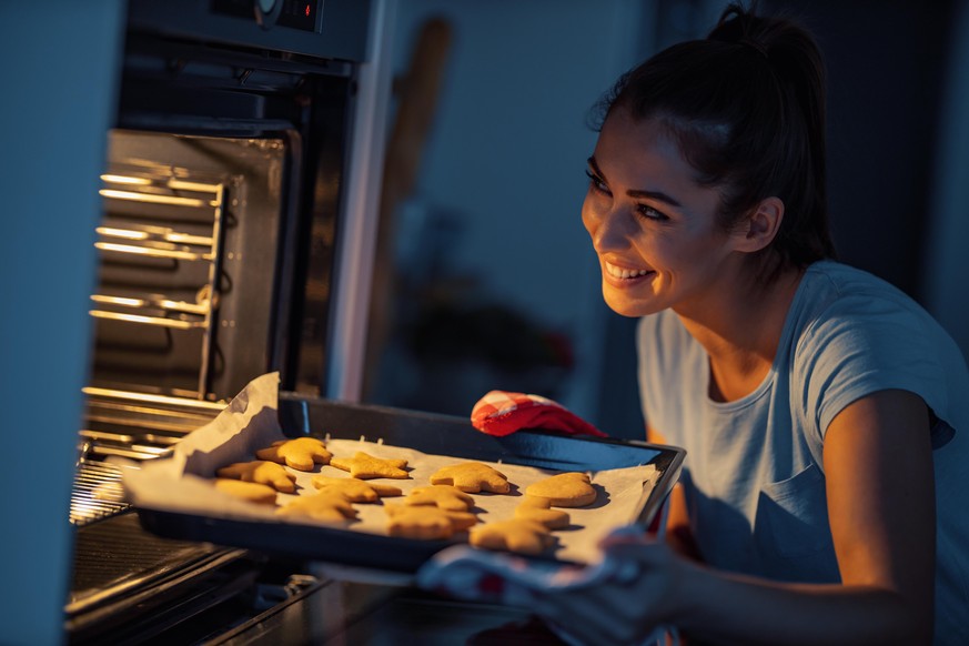 Woman puts gingerbread cookies in the oven.