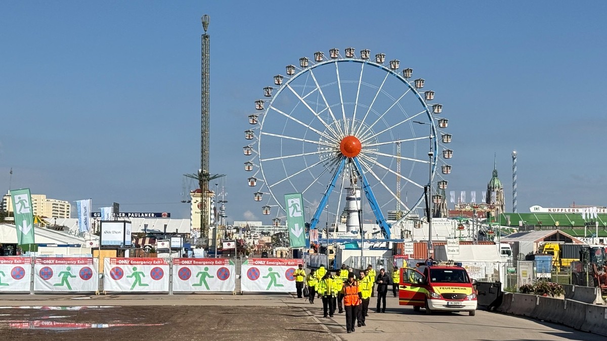 01.10.2025, Bayern, München: Sicherheitskräfte und Einsatzkräfte der Feuerwehr stehen vor dem Gelände vom Oktoberfest (Bestmögliche Qualität). Im Hintergrund ist das Riesenrad zu sehen. Das Münchner O ...