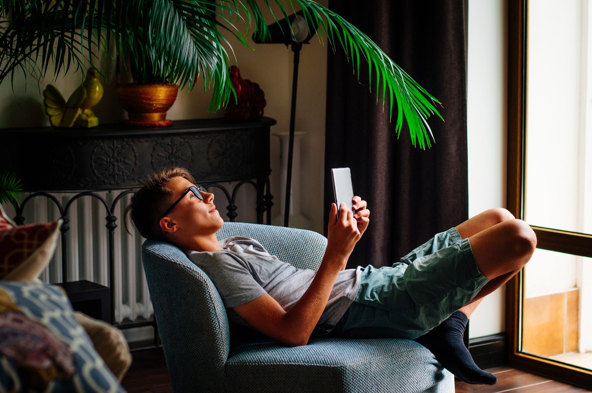 Generation Z concept. Smiling teenager boy using tablet sitting in the chair indoor.