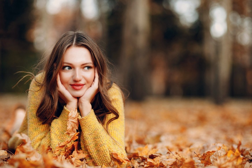 Young woman lies in autumn park ground with yellow foliage maple leaves around