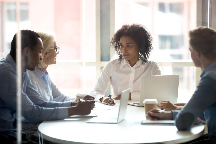 Serious african american female leader talking at diverse group boardroom meeting, multi-ethnic team people employees discussing deal benefits, negotiating on business contract terms with clients