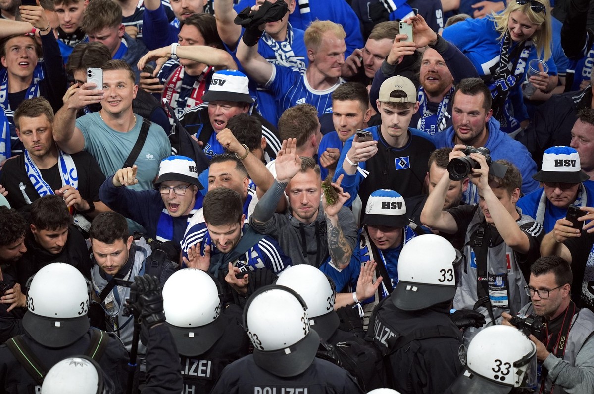 10.05.2025, Hamburg: Fu�ball: 2. Bundesliga, Hamburger SV - SSV Ulm 1846, 33. Spieltag, Volksparkstadion. Ein Hamburger Fan h�lt ein St�ck Rasen in der Hand, w�hrend Polizisten vor den HSV-Fans stehen ...