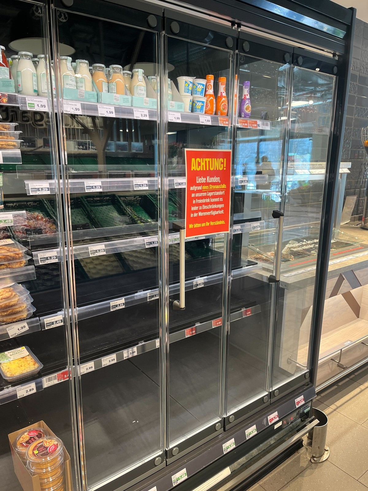Berlin-Mitte: Der halbe Kühlschrank im Edeka ist leer, vorne klebt ein Hinweis auf die Lieferprobleme.