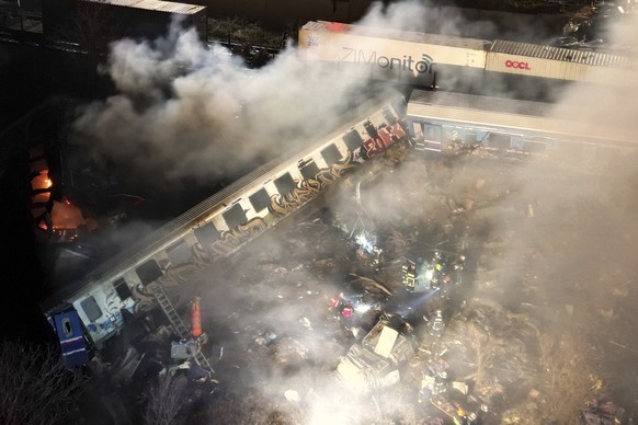 01.03.2023, Griechenland, Larissa: Rauch steigt auf, während Feuerwehrleute und Rettungskräfte nach einem Zusammenstoß zweier Züge in der Nähe von Larissa im Einsatz sind. Mindestens 15 Menschen sind  ...