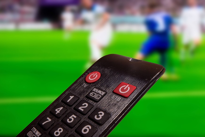 Nahaufnahme einer Fernbedienung, im Hintergrund läuft ein Spiel der Fußball-Weltmeisterschaft in Katar Symbolbild *** Close up of a remote control, in the background a match of the soccer world cup in ...