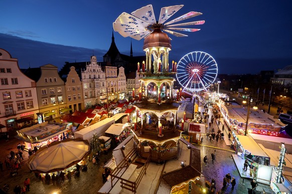 21.11.2022, Mecklenburg-Vorpommern, Rostock: Nach der Eröffnung des Weihnachtsmarktes sind Besucher auf dem Neuen Markt vor der Marienkirche unterwegs, eine große Weihnachtspyramide überragt alles. De ...