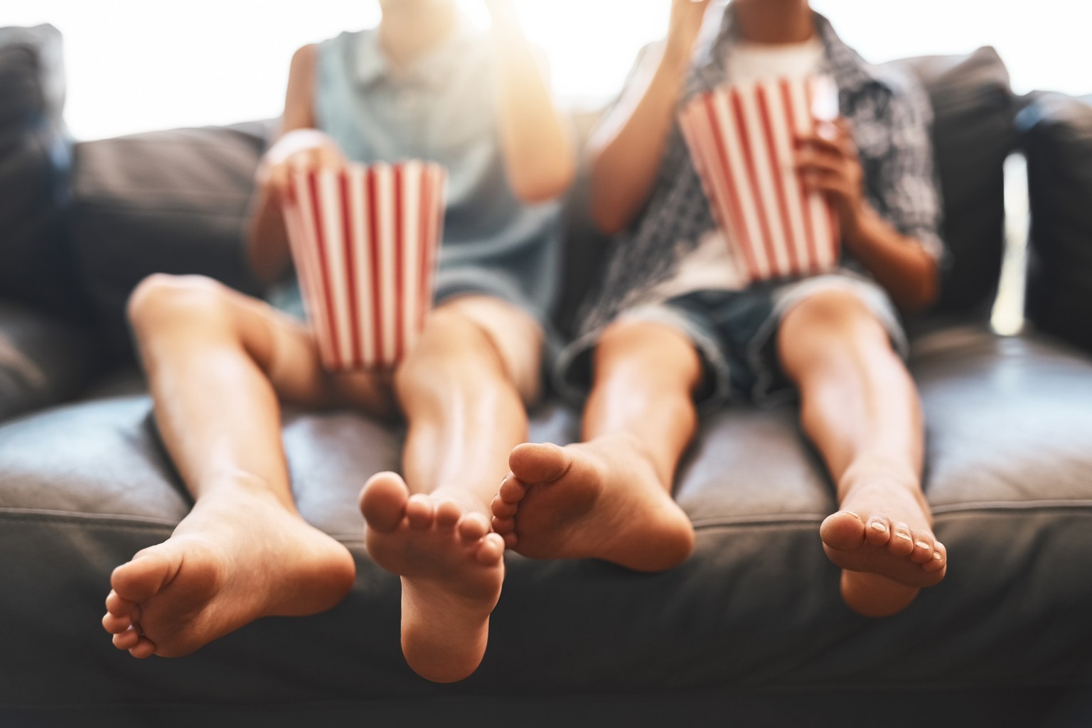 Cropped shot of a brother and sister eating popcorn and watching movies on the sofa at home