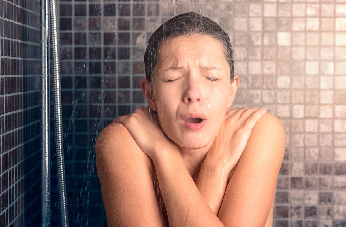 Close up Bare Young Woman Reacting While Taking Cold Shower with Arms Crossing Over her Chest and Eyes Closed.