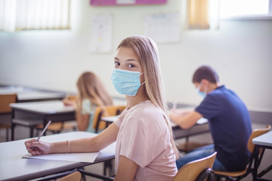 Portrait of school girl. Teenagers students sitting in the classroom. Girl looking at camera. Focus is on foreground.