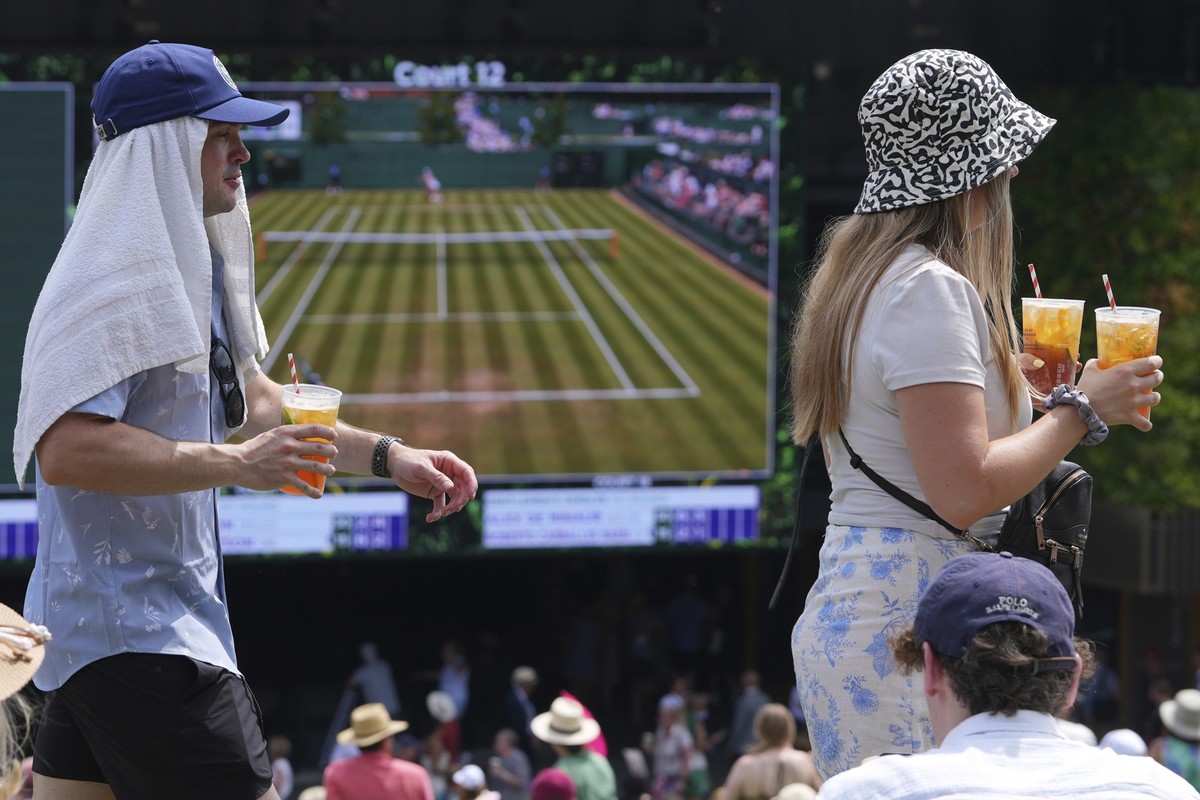 01.07.2025, Großbritannien, London: Während der Wimbledon Tennis Championships in London gehen Zuschauer bei Hitze mit Getränken vorbei, während andere Tennis auf Großbildschirmen auf dem &quot;Hill&q ...