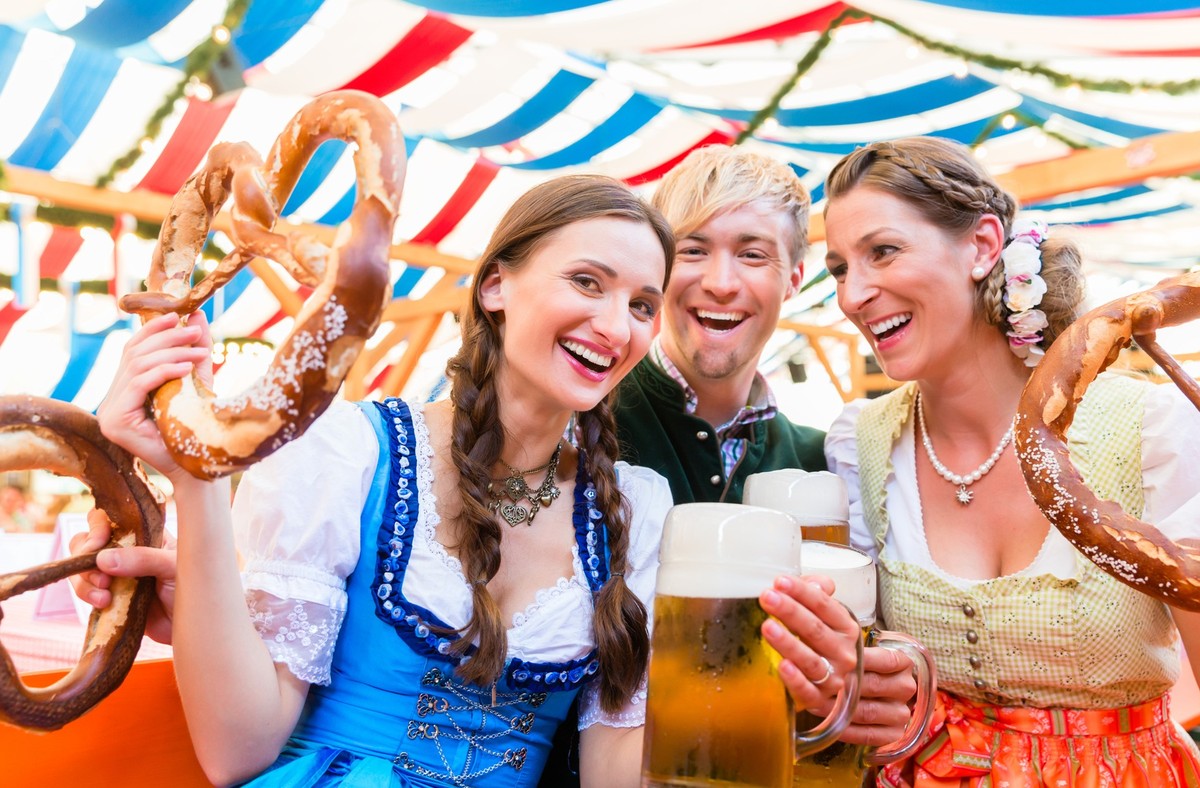 Three friends in beer tent at Dult or Beer Fest holding giant pretzels up in the air