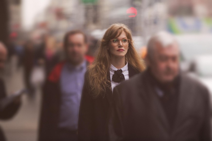 a red haired business woman is walking through a crowded shopping street among the blurred vivid city, all the focus is concentrated on her, as the rest of the environment and peoples are completely b ...