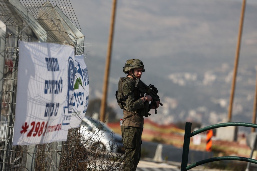 26.02.2023, Palästinensische Gebiete, Kfar Tapuach: Ein Polizist steht Wache, während israelische Sicherheitskräfte die Straße sperren und nach einem Schusswechsel im Gebiet Hawara nach dem Schützen s ...