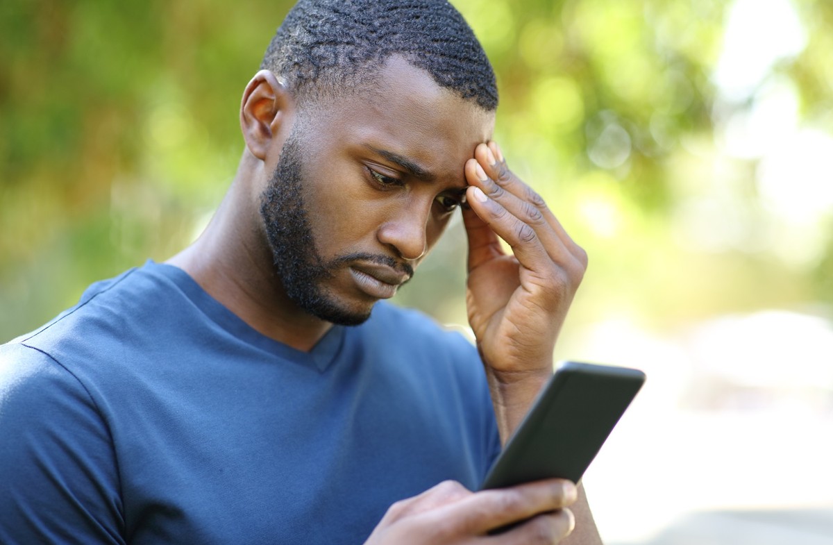 Worried black man checking smart phone in a park