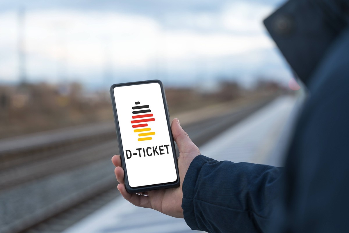 Augsburg, Bavaria, Germany - 28 April 2023: A man stands at the train station holding a smartphone with the D-Ticket Deutschlandticket app. The Deutschland Ticket also called 49 Euro Ticket is the suc ...