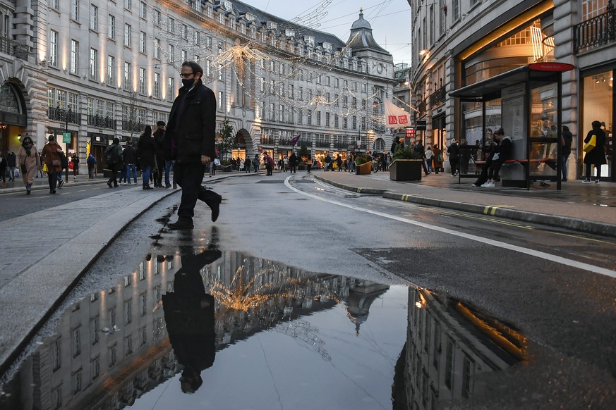 A man wears a face mask while he walks and is reflected into a puddle in Regent Street, ahead of the new Tier-4 restriction measures, in London, Saturday, Dec. 19, 2020. Britain&#039;s Prime Minister  ...