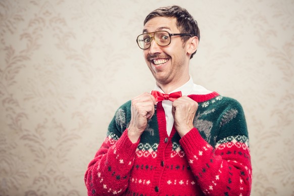 A man in a knit reindeer Christmas cardigan button up sweater, complete with matching red bow tie and a classy mustache. He straightens his bow tie with a cheesy smile on his face, proud of his fashio ...