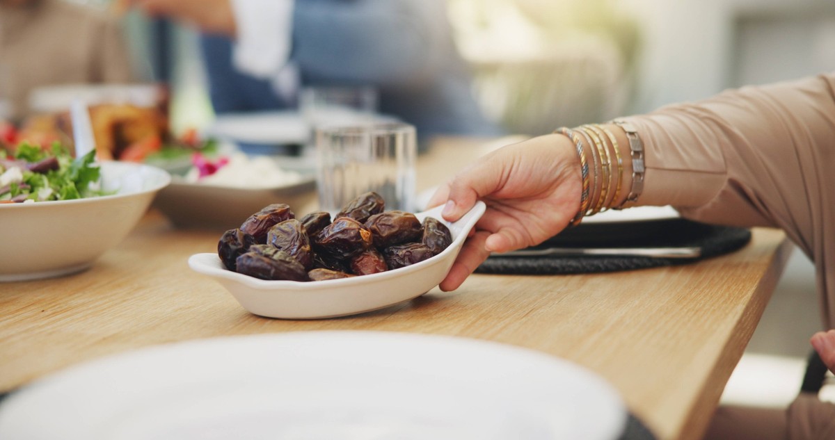 Dates, fruit and hand with bowl on table for dinner or celebration in house with healthy organic choice. Heart health, low blood sugar and cholesterol benefits with vitamins, raw and delicious PUBLICA ...