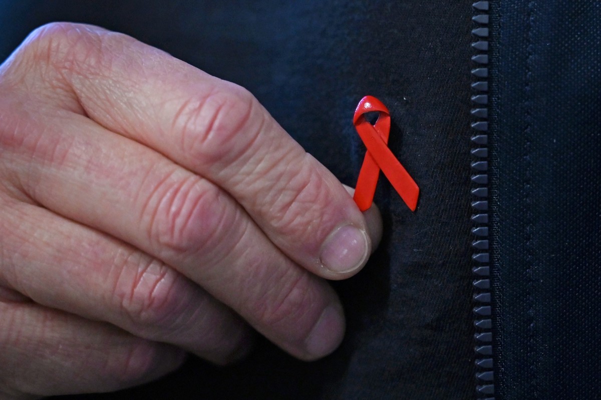 PRODUKTION - 27.11.2025, Berlin: Am Shirt eines Mannes in den Räumen der Berliner Aids-Hilfe e. V. ist eine rote Schleife befestigt, das internationale Symbol der Solidarität mit Menschen, die mit HIV ...