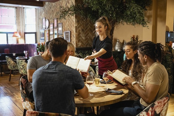 A multi-ethnic group of friends looking at menus together in a restaurant, which have been given to them by a waitress.