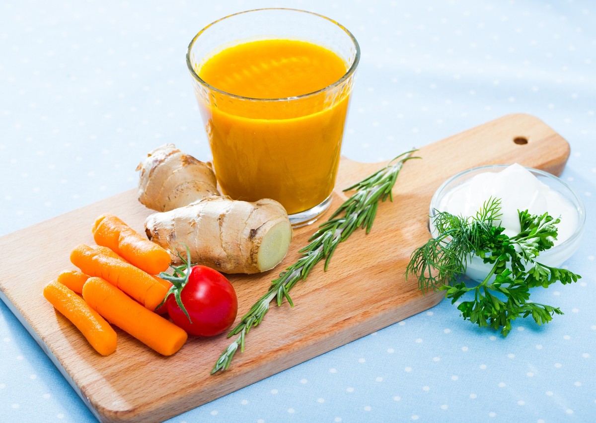 Freshly squeezed carrot juice served with ginger, fresh vegetables and cream on wooden board