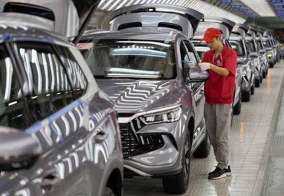 ARCHIV - 24.04.2024, China, Zhengzhou: Ein Arbeiter pr�ft die Qualit�t eines New Energy Vehicle (NEV) im Werk von BYD, Chinas f�hrendem NEV-Hersteller, in Zhengzhou in der zentralchinesischen Provinz  ...