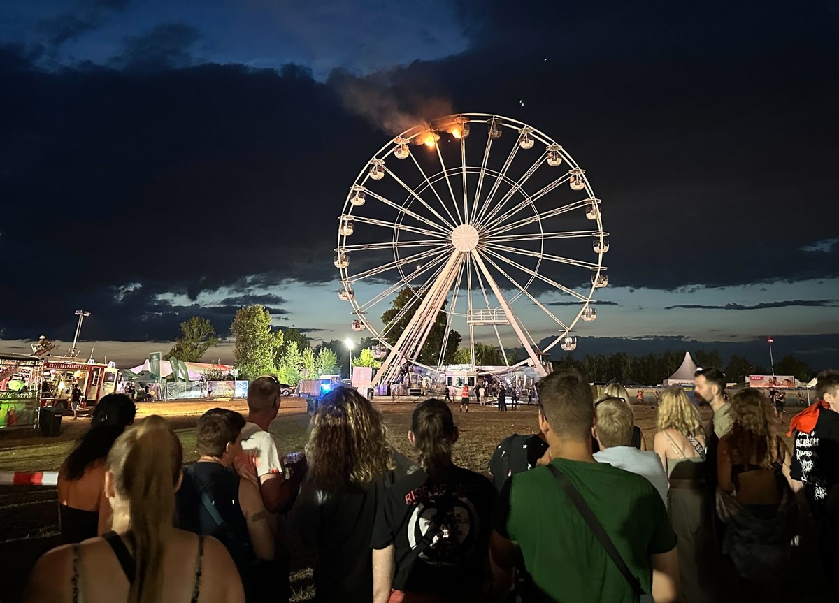 17.08.2024, Sachsen, Gro�p�sna: Besucher des Highfield-Festivals blicken auf ein�Riesenrad, an dem Flammen zu sehen sind. 

Menschen beobachten, wie zwei Gondeln eines Riesenrads brennen. (zu dpa: �Na ...