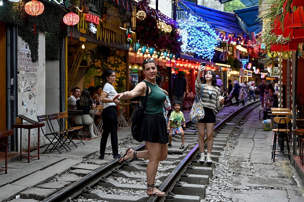 This photo taken on August 18, 2025 shows a tourist posing for a photo along a railway track between cafe terraces in central Hanoi. Coffee-roused tourists snap selfies at Hanoi&#039;s softly-lit rail ...