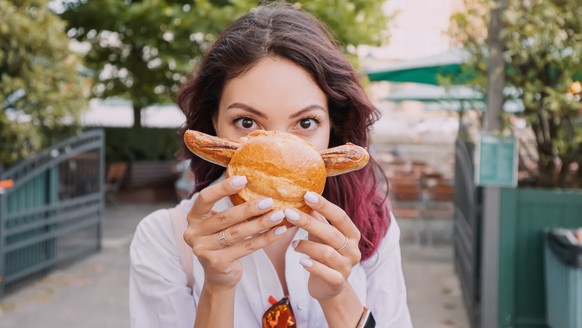 A happy girl eats an appetizing traditional German bratwurst hot dog with juicy sausage and seasonings