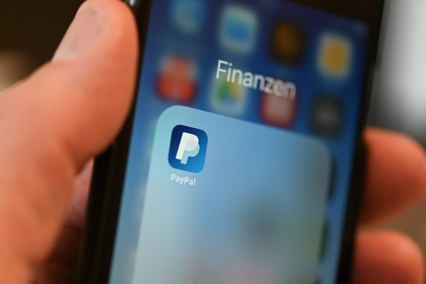 ARCHIV - 29.07.2020, Baden-Württemberg, Ravensburg: Die Applikation von PayPal ist auf einem Mobilfunkgerät zu sehen, das ein Mann in der Hand hält. Beim Online-Shopping bezahlt die deutschen Kundscha ...