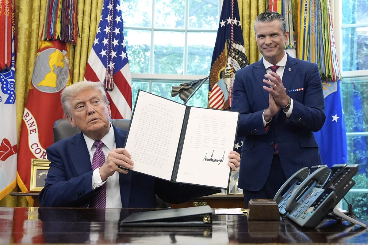 President Donald Trump holds top a signed executive order as Defense Secretary Pete Hegseth watches in the Oval Office of the White House, Friday, Sept. 5, 2025, in Washington. (AP Photo/Alex Brandon)