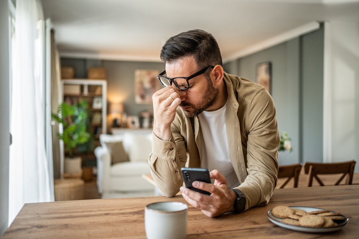 A young man is feeling depressed and thinking about the bad news he is reading online through his smartphone