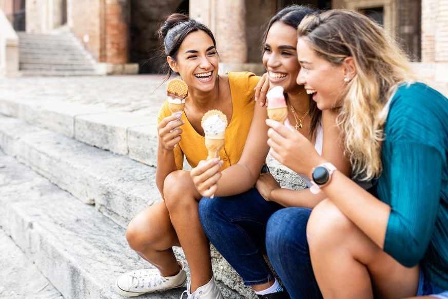 Drei ziemlich multirassische glückliche Frauen, die sich unterhalten und Eis essen, während sie an der Treppe sitzen - Freundschaft und Sommerurlaub in Italien Konzept