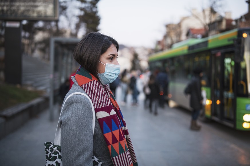 Eine Frau an einer Bushaltestelle trägt einen Nasen-Mund-Schutz.