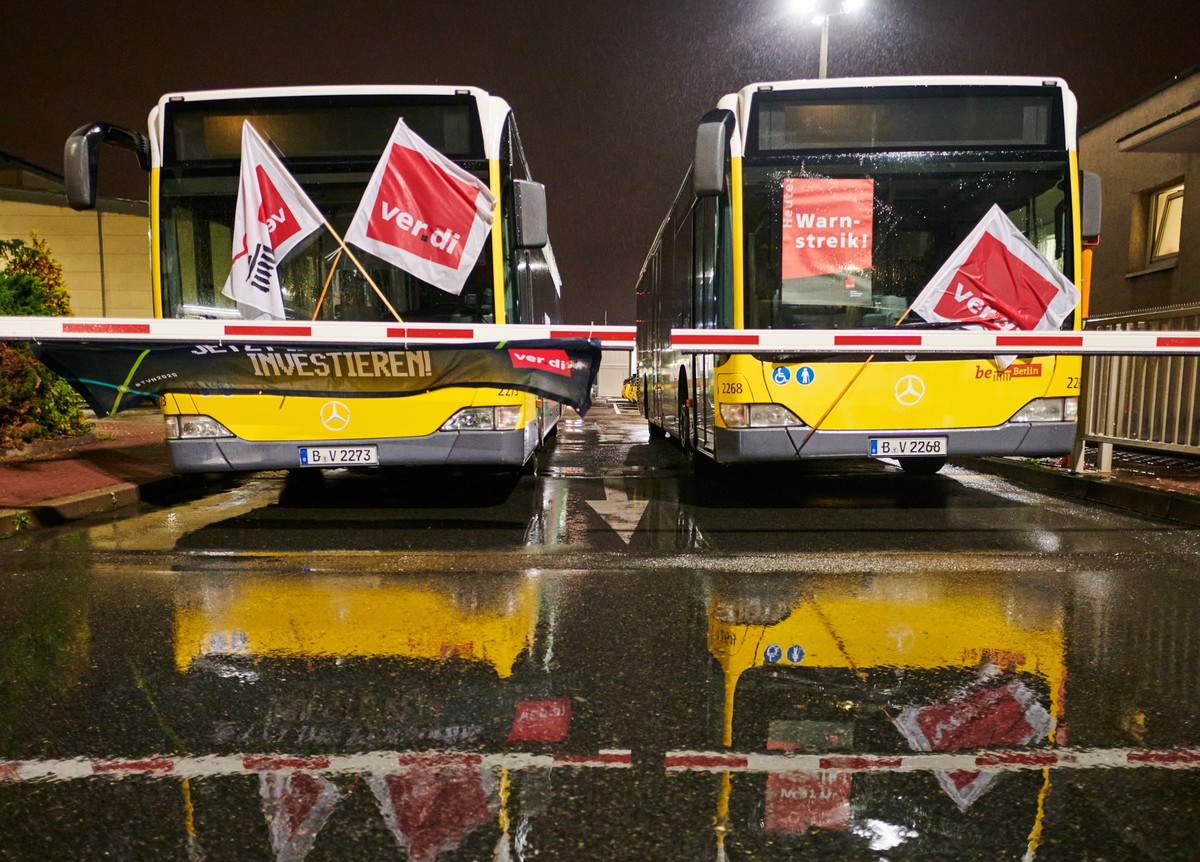 ARCHIV - 09.10.2020, Berlin: Busse mit Verdi-Fahnen stehen hinter einer Schranke an der Einfahrt zum Betriebshof der Berliner Verkehrsbetriebe (BVG) in Lichtenberg. Im