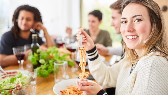 Freunde essen gemeinsam Spaghetti mit Tomatensauce in der Küche einer WG